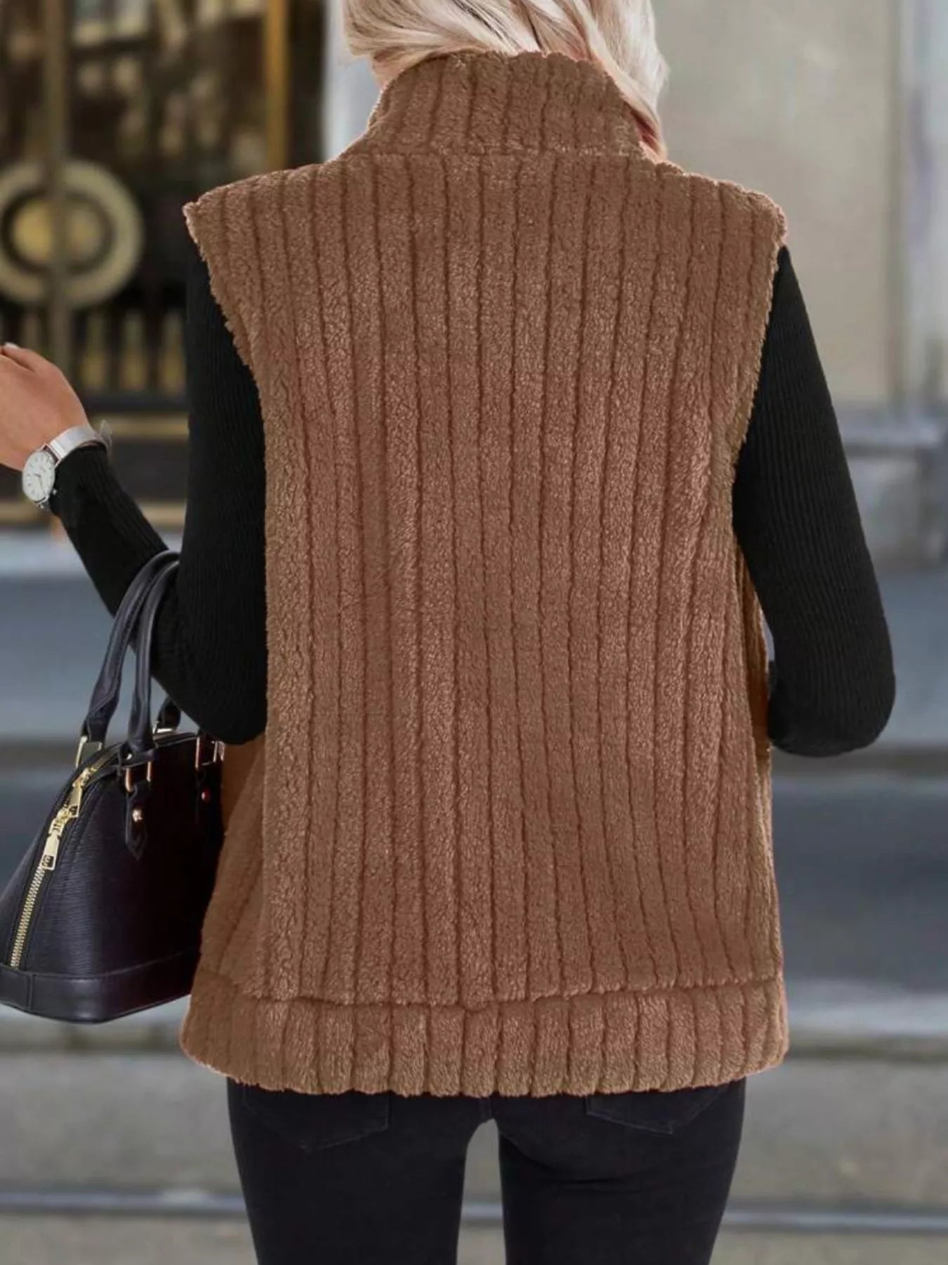 Brown fleece zip-up vest with vertical ribbing and stand-up collar, worn over a black long-sleeve shirt.