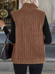 Brown fleece zip-up vest with vertical ribbing and stand-up collar, worn over a black long-sleeve shirt.