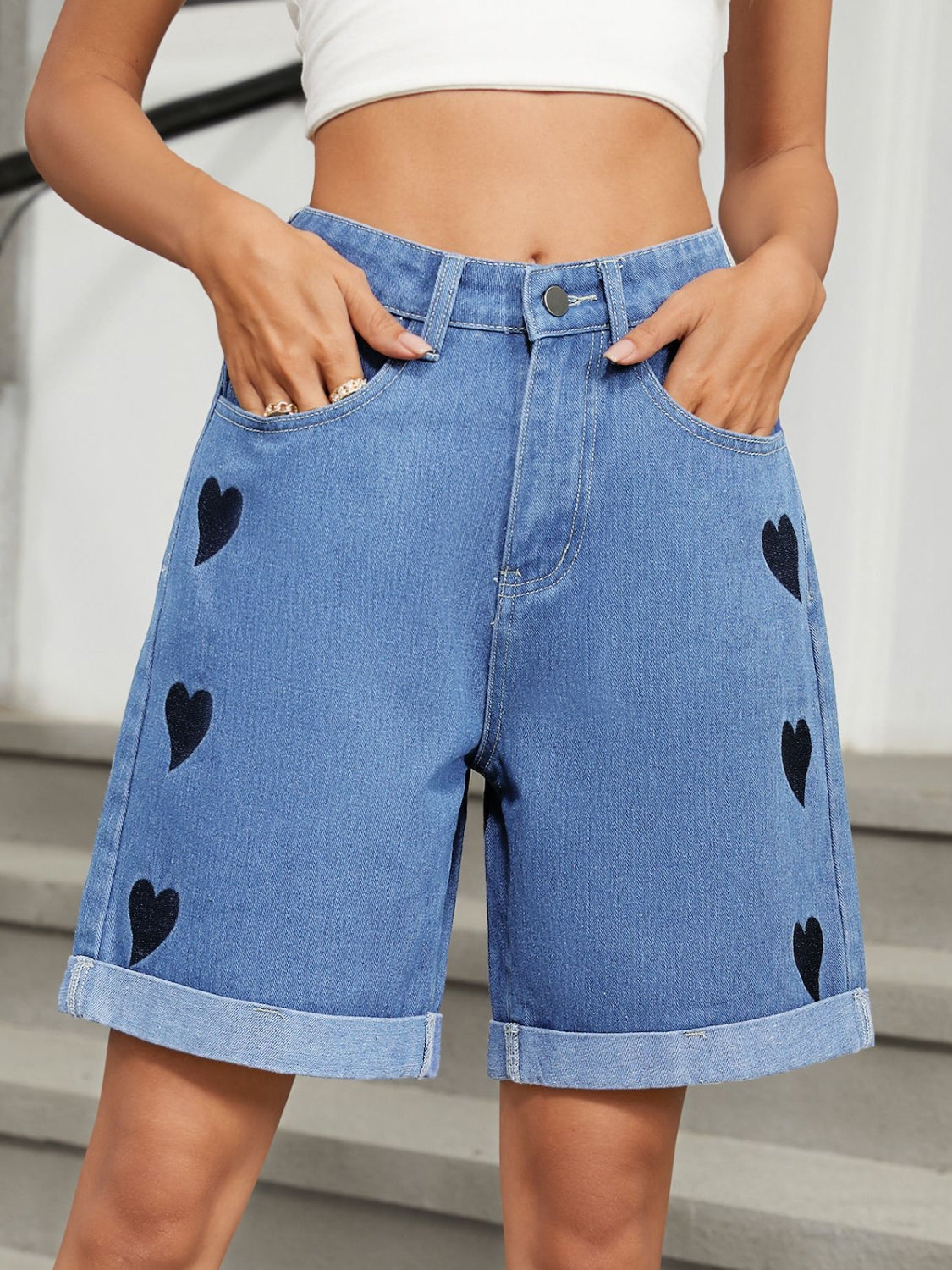 Medium wash denim bermuda shorts with black heart appliqués and cuffed hems.