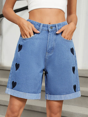 Medium wash denim bermuda shorts with black heart appliqués and cuffed hems.