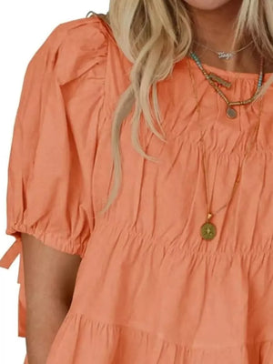 Orange maternity blouse with puff sleeves, ruffled tiers, and tie details.