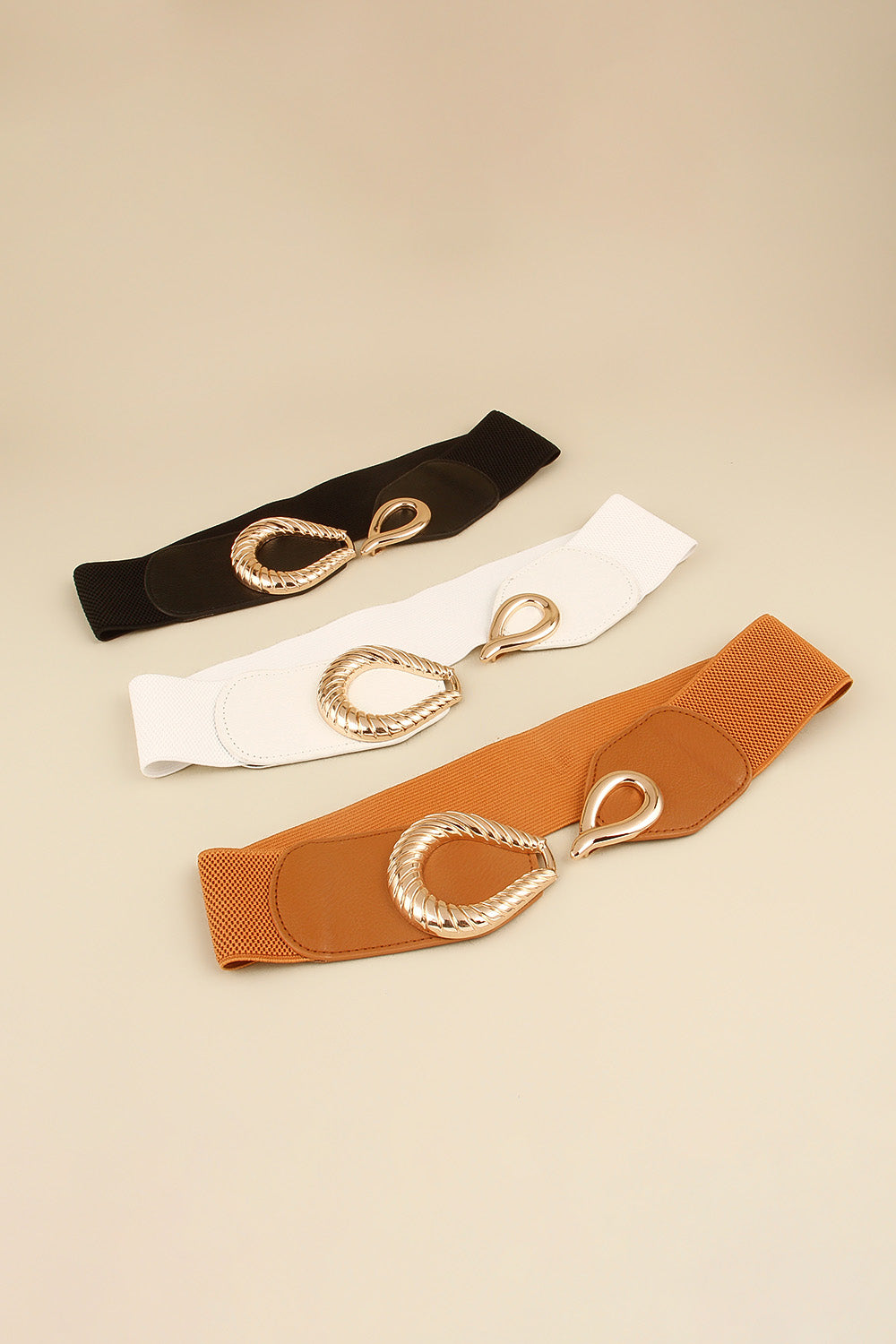 Elasticated waist belts in black, white, and caramel with sculpted gold alloy buckles.