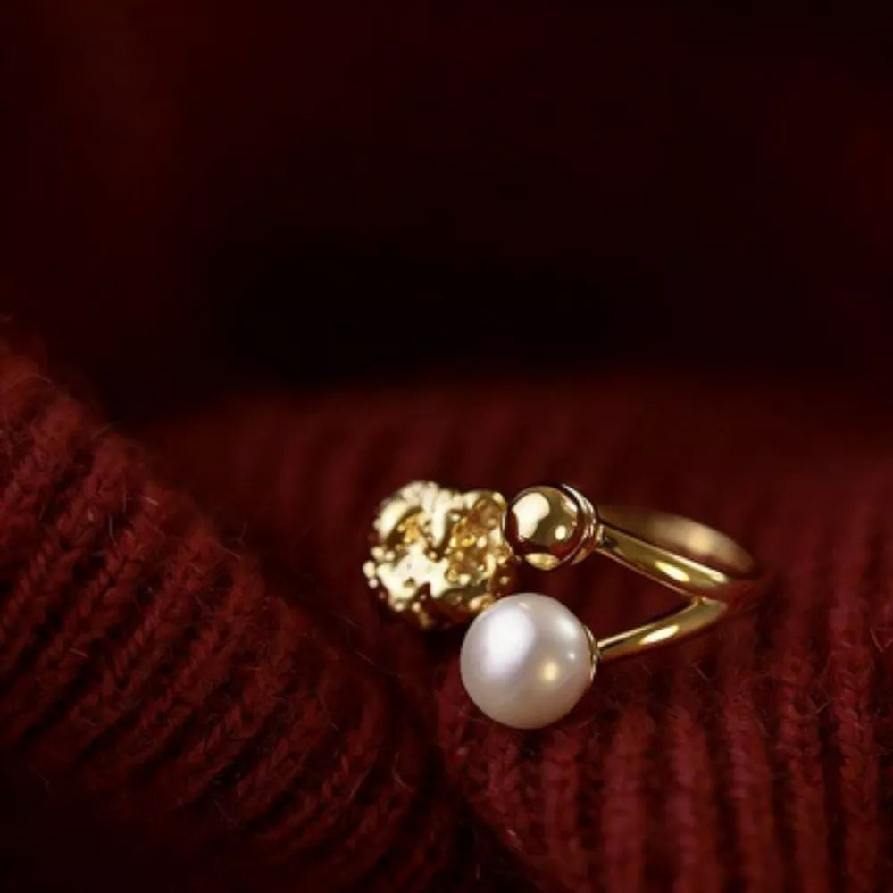 Gold open ring with pearl and textured gold detail on red fabric.
