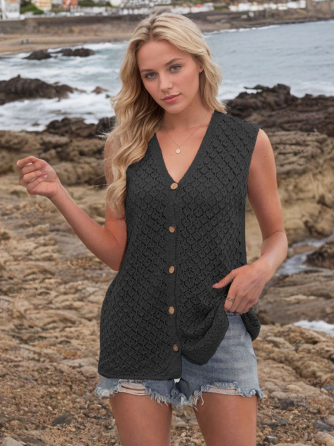 Black openwork knit vest with V-neck and button front, styled with denim shorts.