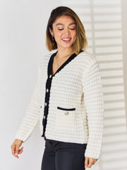 White textured knit cardigan with black contrast trim and buttons, featuring a patch pocket.