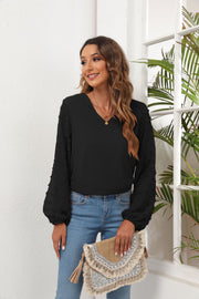 Black V-neck blouse with textured pom-pom detail on balloon sleeves.