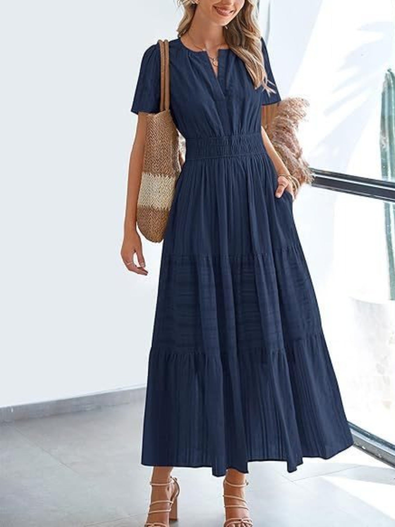 Dark navy V-neck tiered maxi dress with smocked waist and short sleeves, styled with a straw bag.