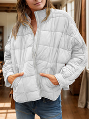 White quilted bomber jacket with stand collar and zip front, hands in pockets.