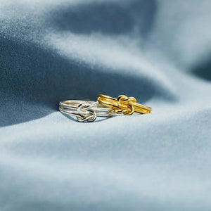Double band knot rings in gold and silver on blue fabric.