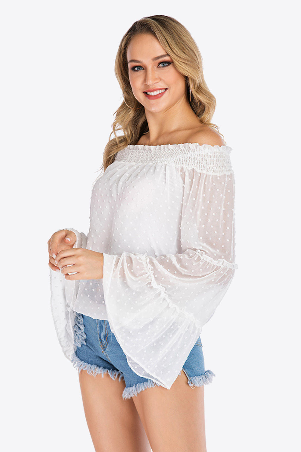 White dotted swiss off-shoulder blouse with ruffle bell sleeves and smocked neckline.