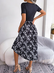 Botanical pleated midi dress in black with a white leaf print, featuring a ribbed bodice and short sleeves.