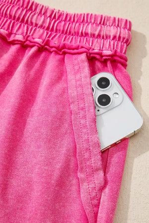 Acid-washed hot pink cotton drawstring shorts with pockets, showing a phone in the pocket.