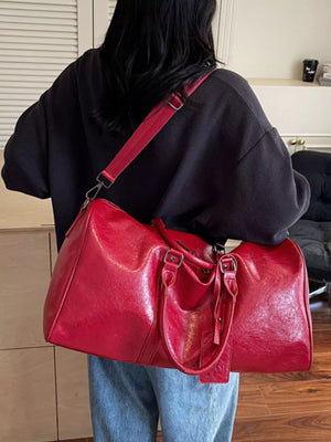 Textured metallic duffle bag in wine red with detachable strap and top handles.