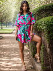 Tropical print wrap romper with short sleeves and tie waist in turquoise and pink.