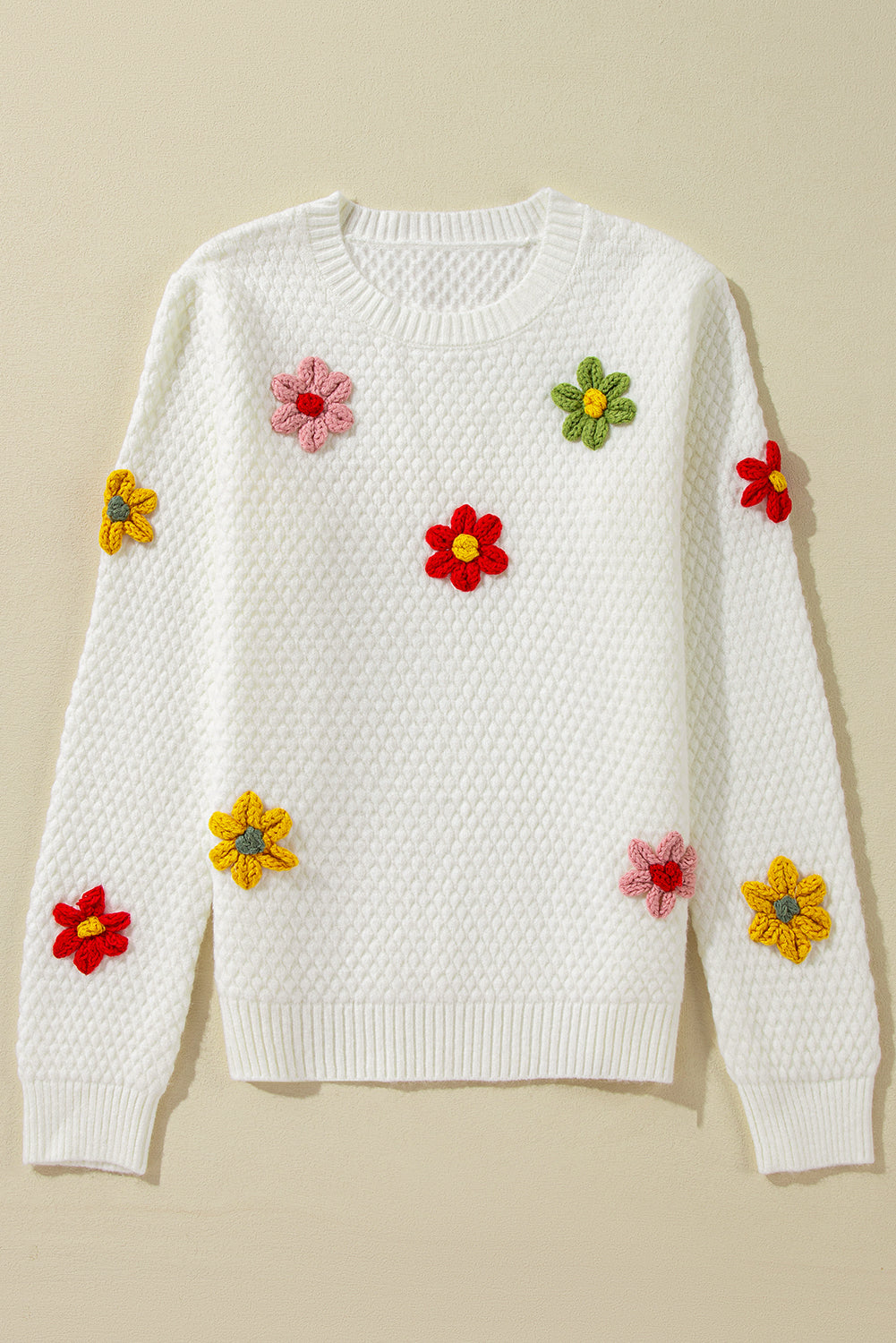 White knit sweater with crochet floral embellishments and a diamond pattern texture.