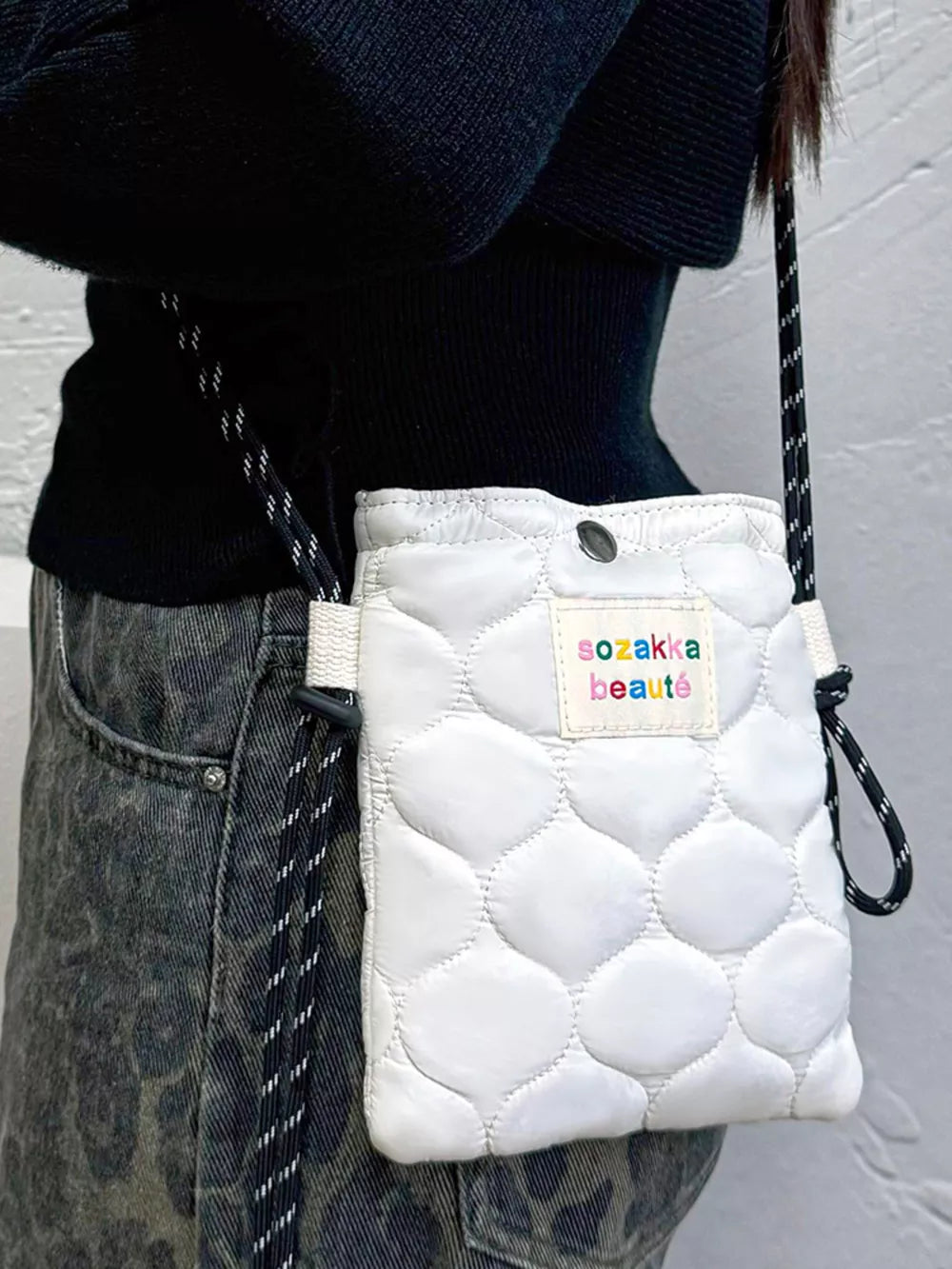 Vibrant quilted mini crossbody bag in ivory with a colorful logo patch and adjustable strap.