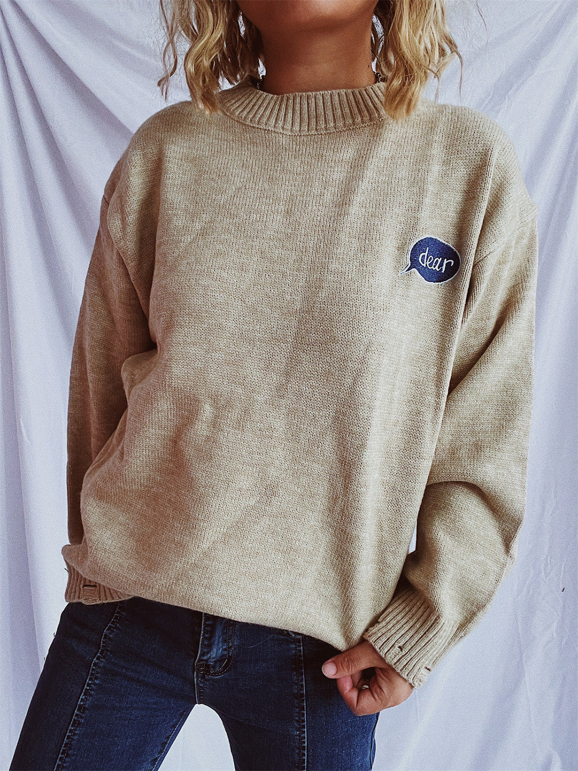 Relaxed knit sweater in dark gray or tan, acrylic, with embroidered character detail.