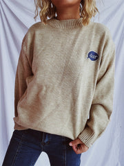 Relaxed knit sweater in dark gray or tan, acrylic, with embroidered character detail.