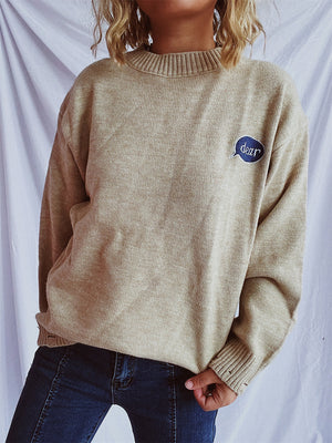 Relaxed knit sweater in dark gray or tan, acrylic, with embroidered character detail.