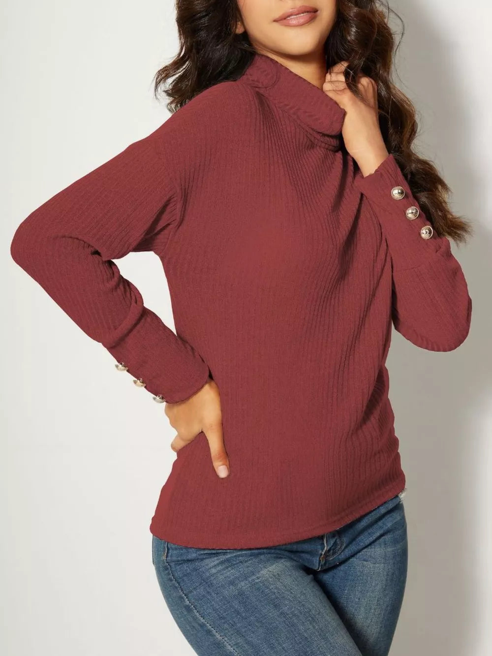 Ribbed turtleneck knit top in brick red with decorative buttons on the cuffs.