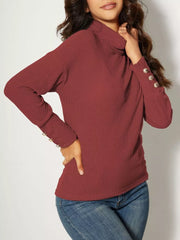 Ribbed turtleneck knit top in brick red with decorative buttons on the cuffs.