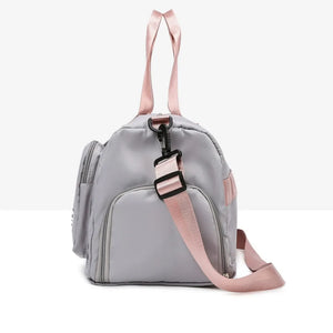 Gray duffel bag with pink straps and buckle detail, side pockets.