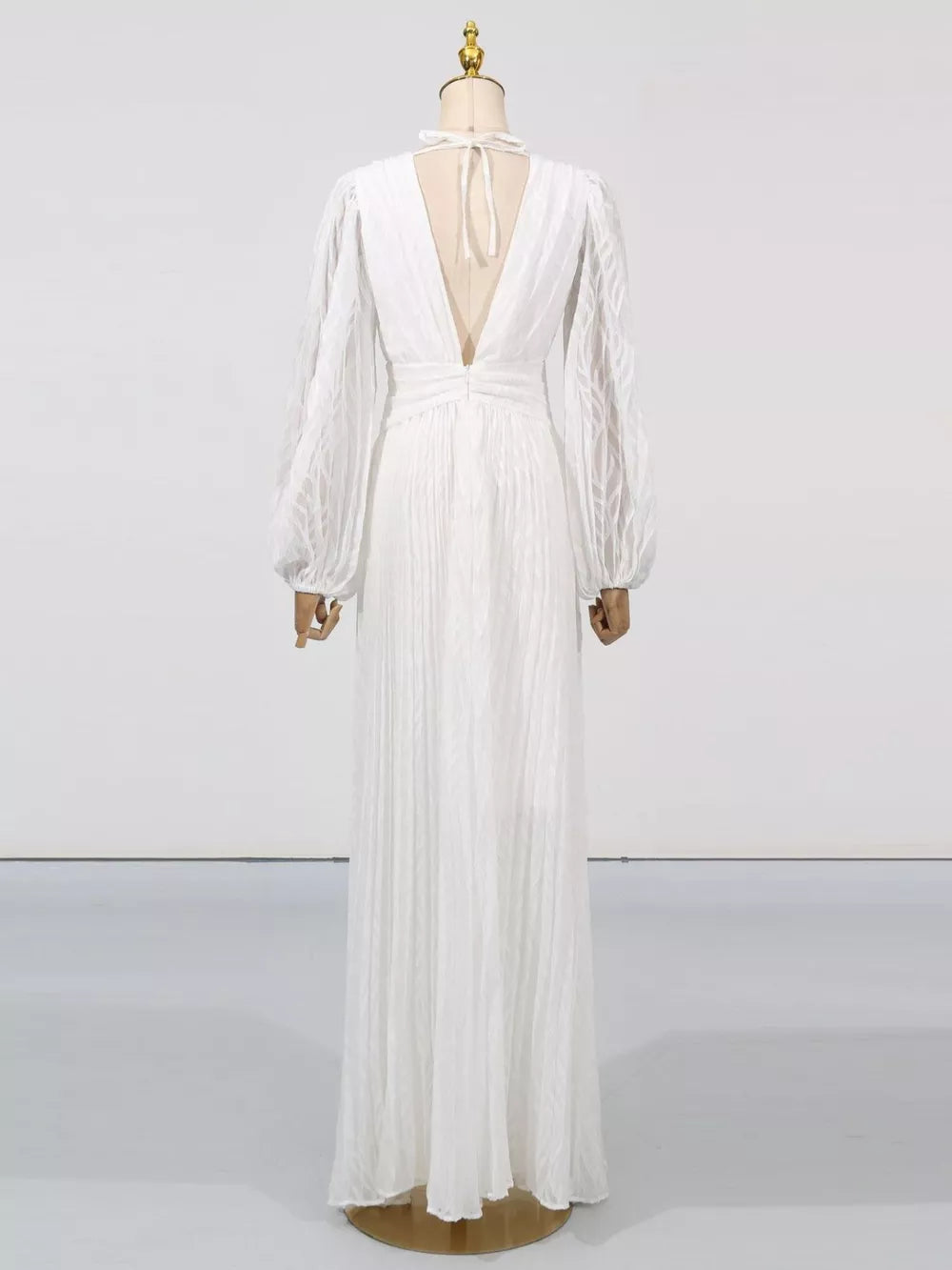 White maxi dress with deep V-back, tie neck, and textured balloon sleeves.