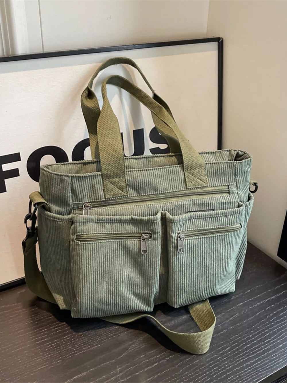 Green corduroy crossbody bag with multiple zippered pockets and top handles.