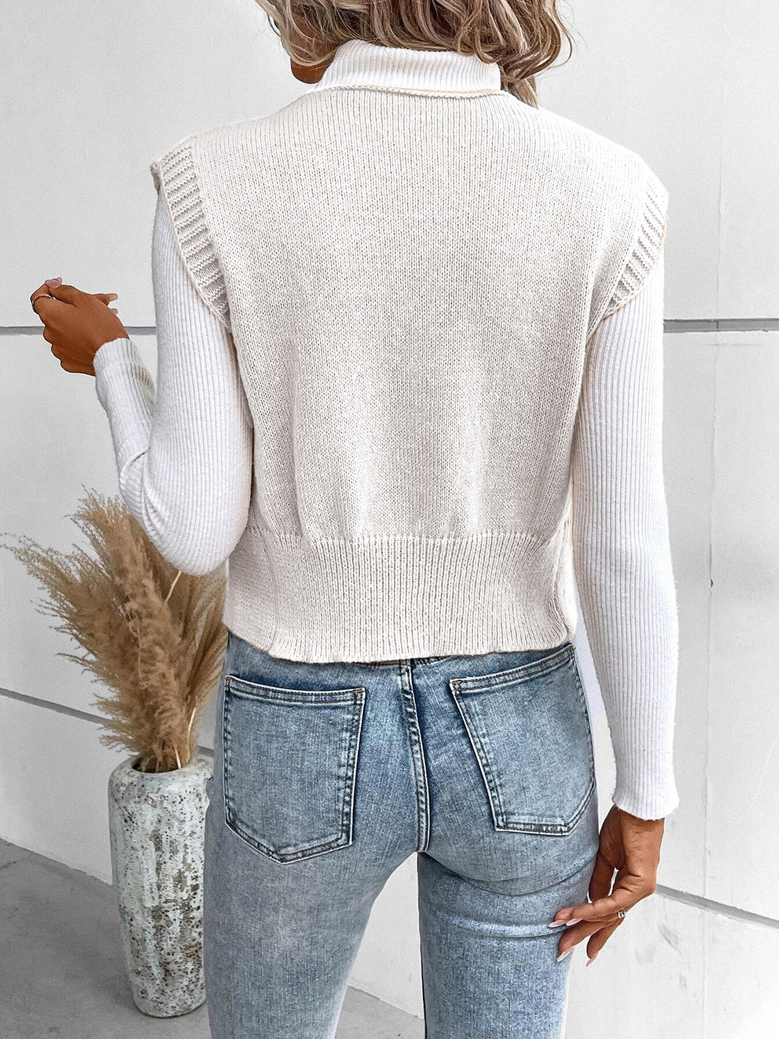 White knit vest with ribbed trim and button detail, worn over a turtleneck.