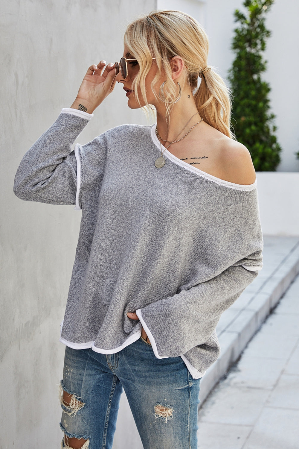 Oversized grey acrylic knit sweater with white contrast trim and off-the-shoulder neckline.