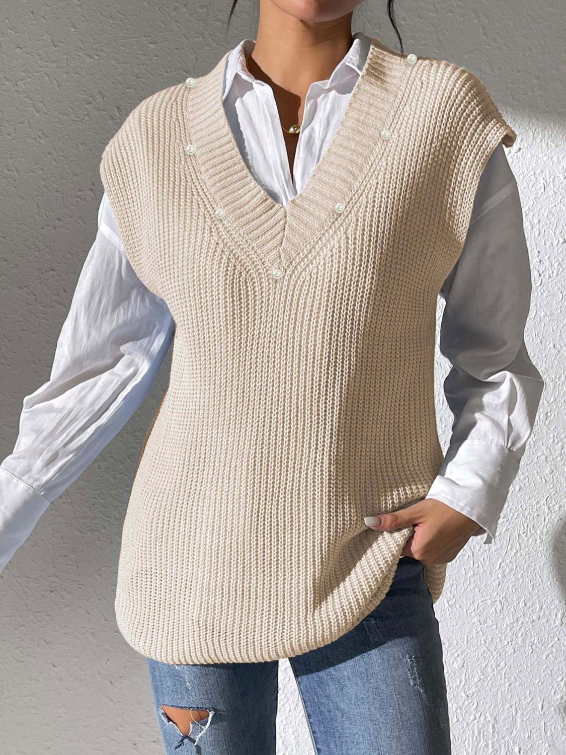 Beige ribbed knit sleeveless v-neck vest with pearl embellishments over a white shirt.
