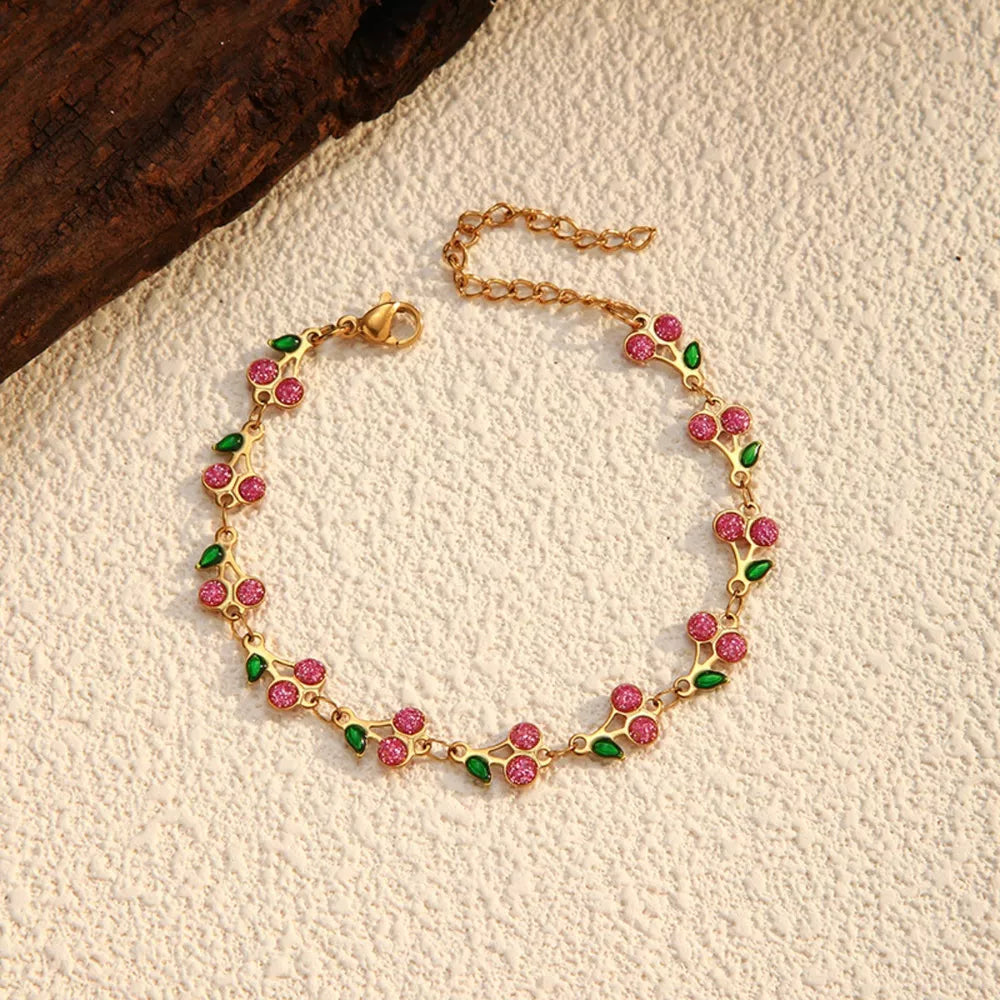 Gold-plated bracelet with pink cherry clusters and green leaves, featuring a delicate chain.