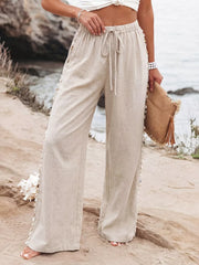 Relaxed beige linen wide-leg trousers with drawstring and shell trim detail.