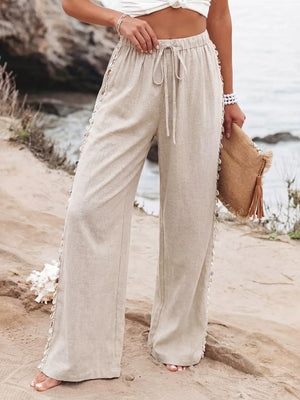 Relaxed beige linen wide-leg trousers with drawstring and shell trim detail.