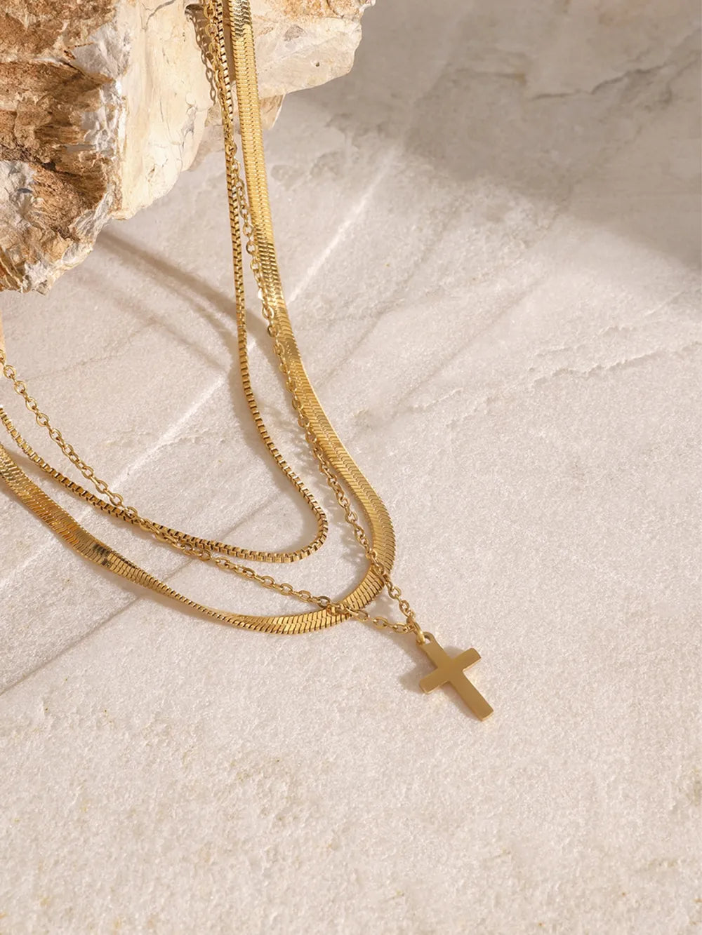 Gold layered necklace with herringbone and snake chains, featuring a small cross pendant.