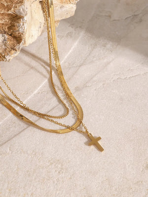 Gold layered necklace with herringbone and snake chains, featuring a small cross pendant.