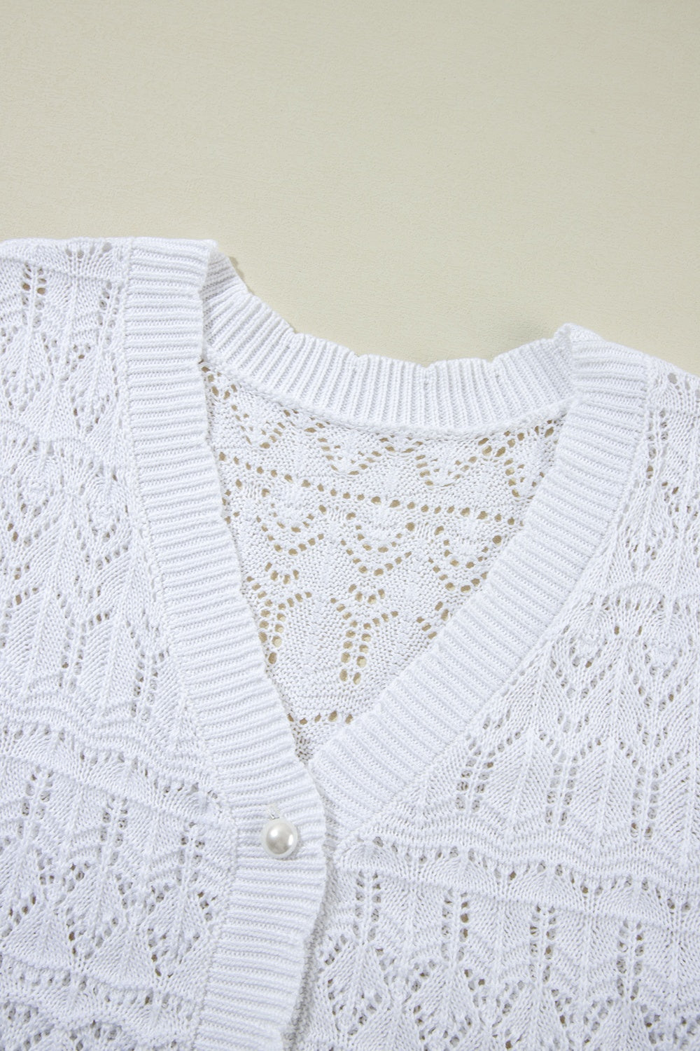 White openwork crochet cardigan with V-neck and pearl button detail.