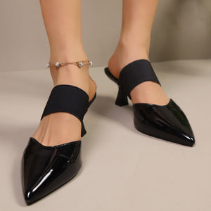 Black patent pointed toe mules with elastic strap and mid heel.