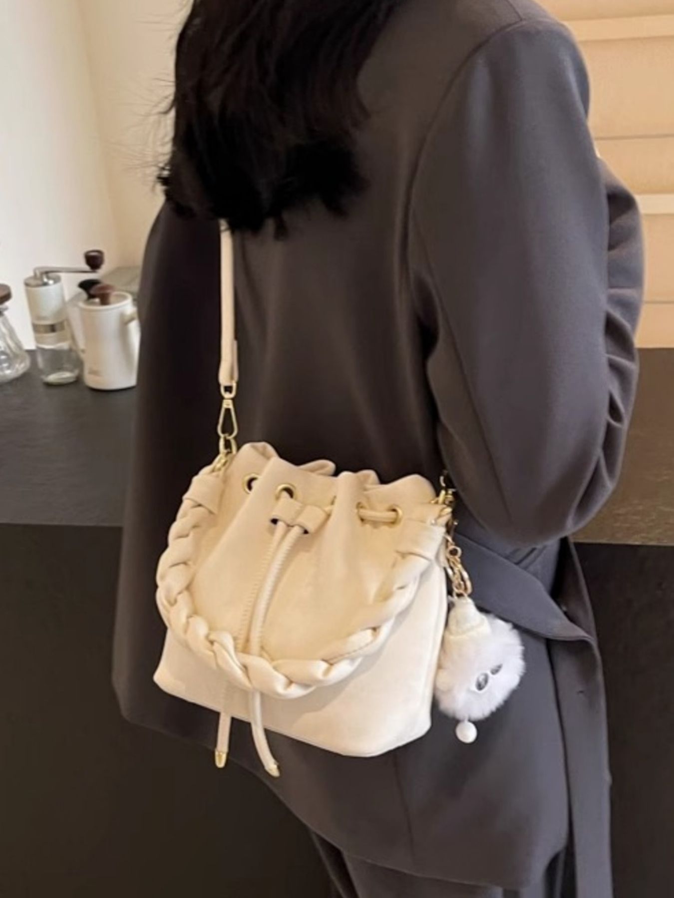 White bucket bag with braided trim, drawstring closure, and fluffy charm.