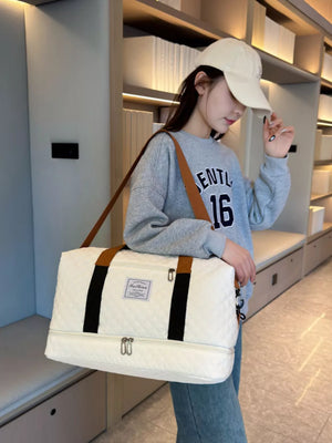 Creamy-white quilted travel duffel bag with dual zippered compartments and brown handles.