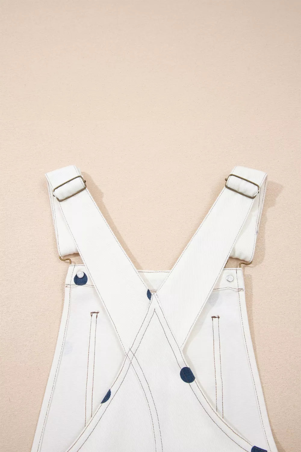White denim overalls with navy polka dots and adjustable straps.