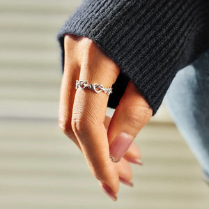 Sterling silver ring with an intertwined heart motif, worn on a finger.