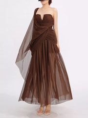 Draped one-shoulder maxi dress in coffee brown with a flowing sheer overlay and ruched bodice.