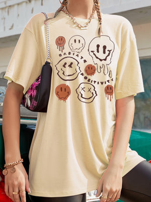 Tan oversized graphic tee with melting smiley faces and "Radiate Positivity" text.