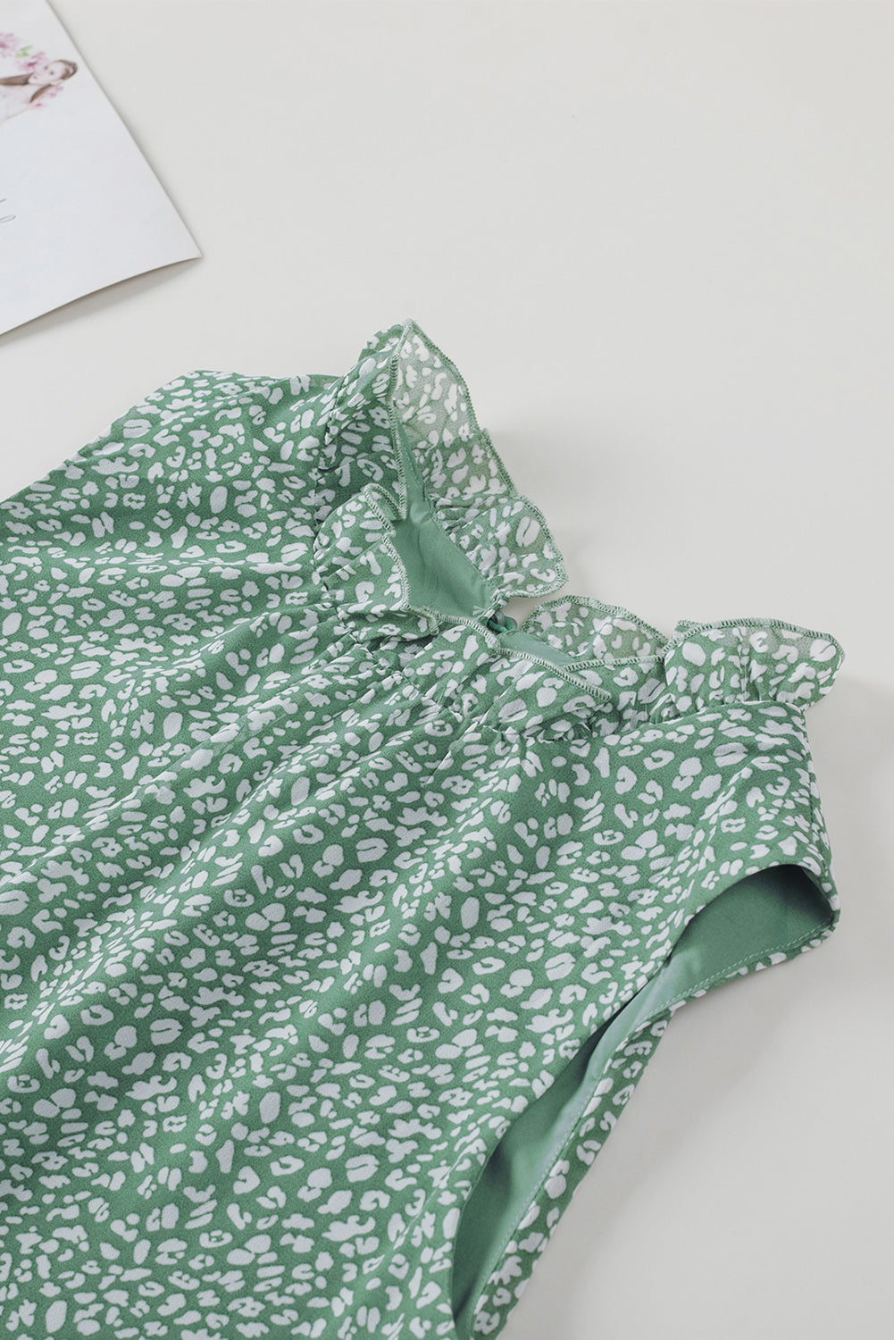 Sage green sleeveless blouse with white leopard print and ruffled neckline.