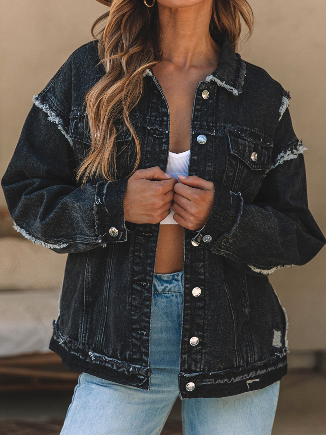 Black denim trucker jacket with raw hem and distressed details.