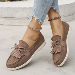 Fringe bow loafer flats in taupe suede with a white sole.