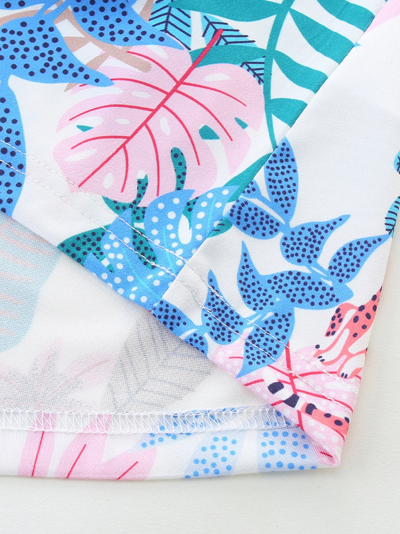 Cotton baby dress with playful tropical leaf print in pink, blue, and green.