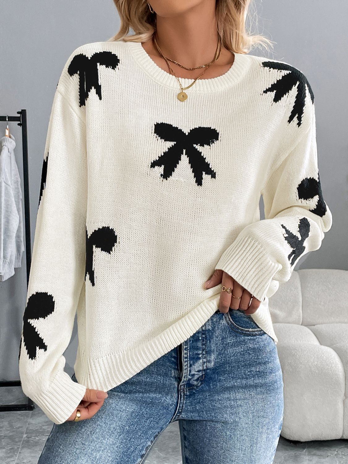 Cream knit crewneck sweater with scattered black bow pattern, long sleeves, and crew neckline.