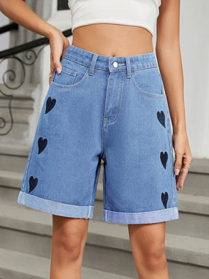 Medium wash denim bermuda shorts with black heart appliqué and cuffed hems.